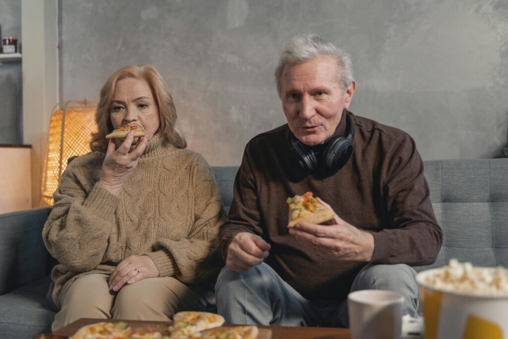 Um casal de idosos comendo uma pizza em casa